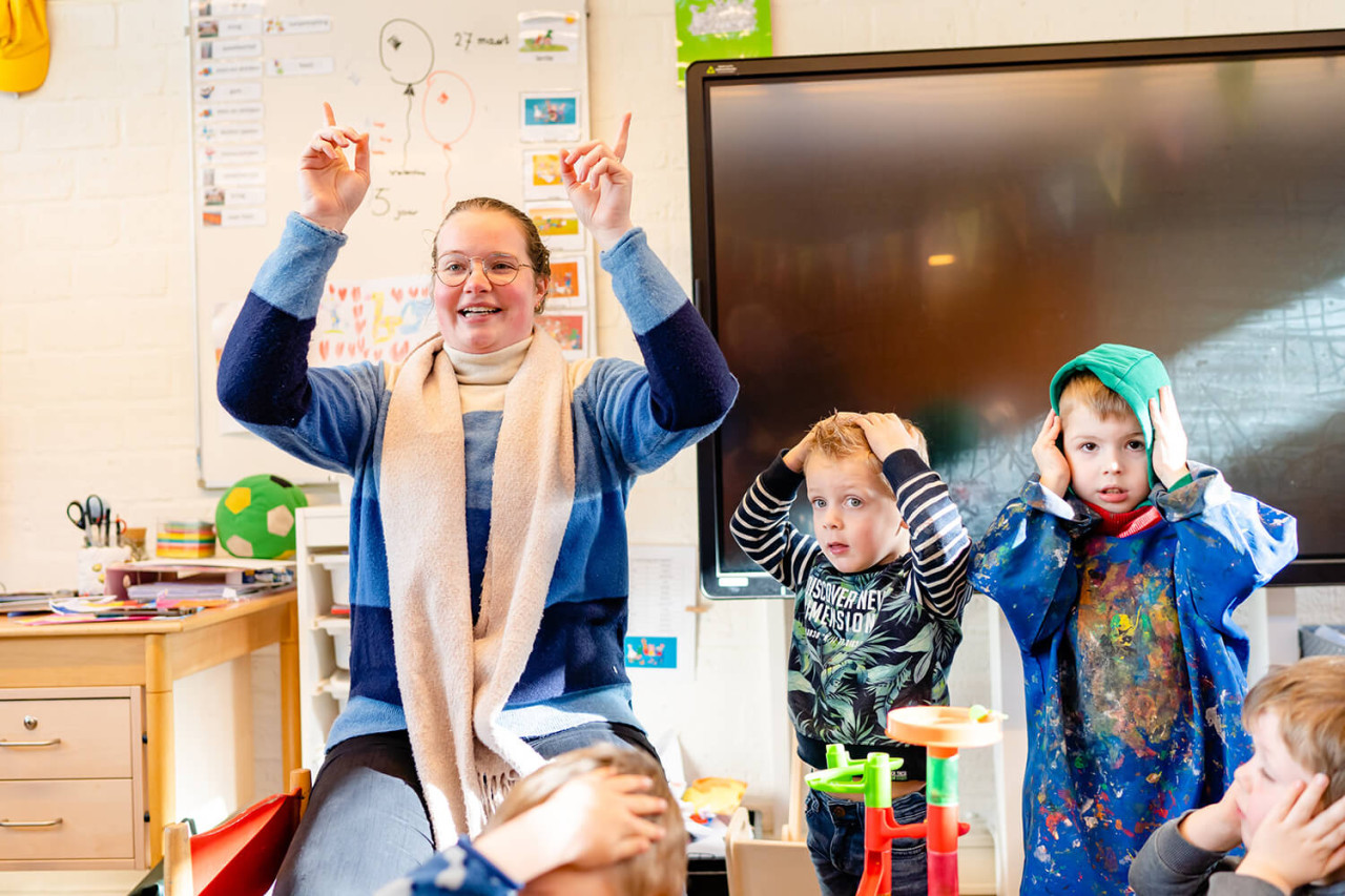Leerkracht met kinderen handen in de lucht