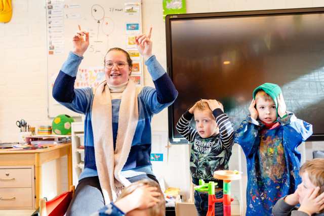 Leerkracht met kinderen handen in de lucht